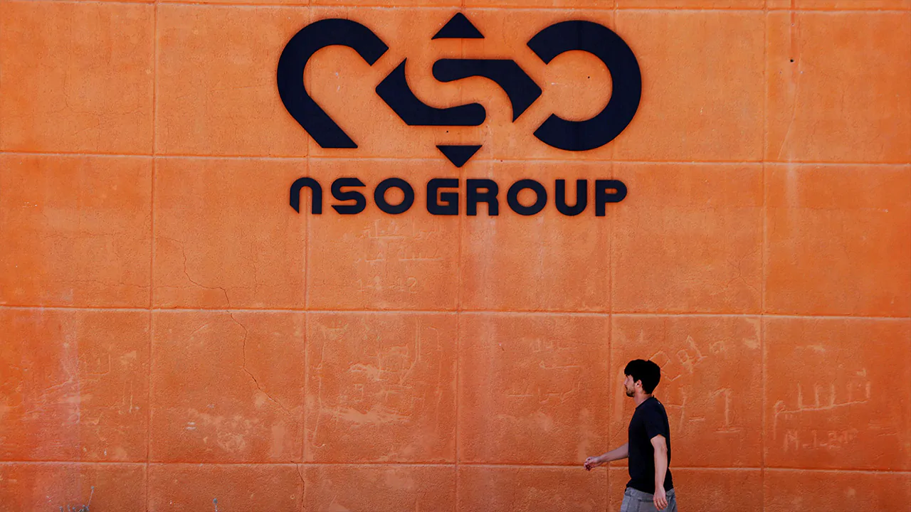 A man walks past a wall with the NSO Group's logo