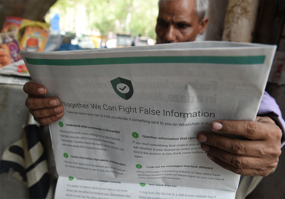 A man reading an Indian newspaper with a full back page advertisement from WhatsApp